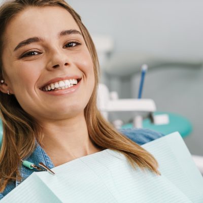 European young woman smiling while sitting in medical chair at dental clinic